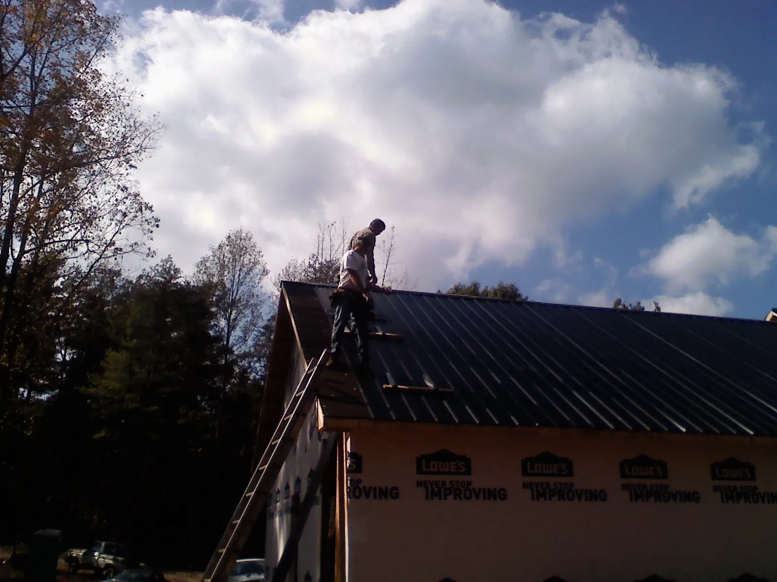 Roofer fastening dark metal panels high against a cloudy sky, from a Roof Inspection job in Granger