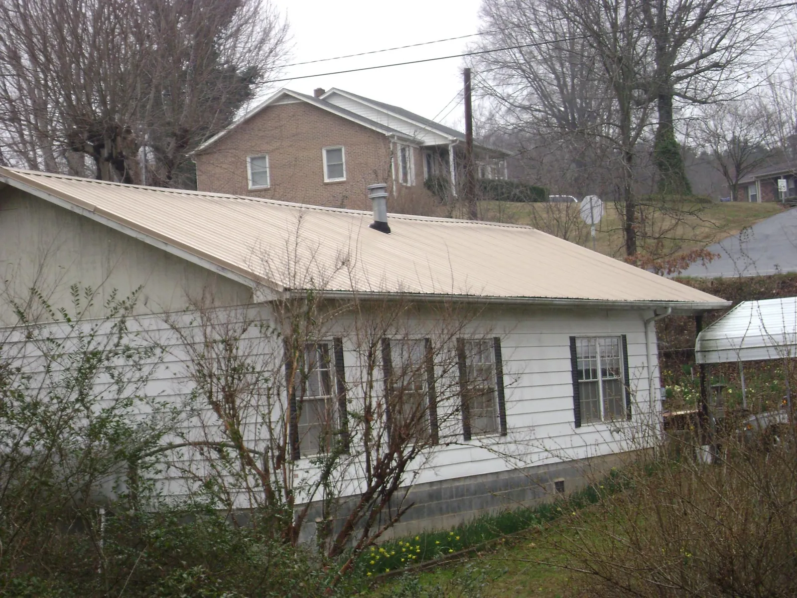 Tan metal roof on a white sided house set into a hillside — Commercial Roofing by Roofing Brothers in Granger