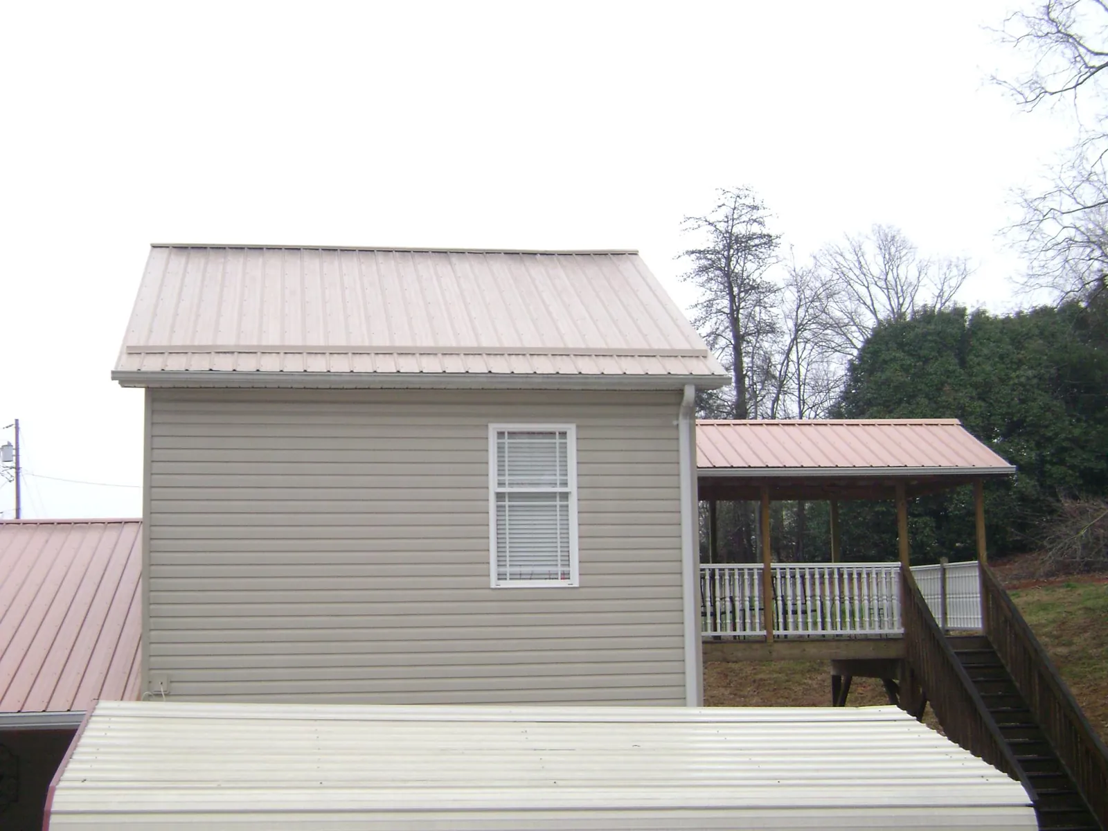 Tan metal roofs on a two story addition and attached porch, from a Roof Replacement job in Granger